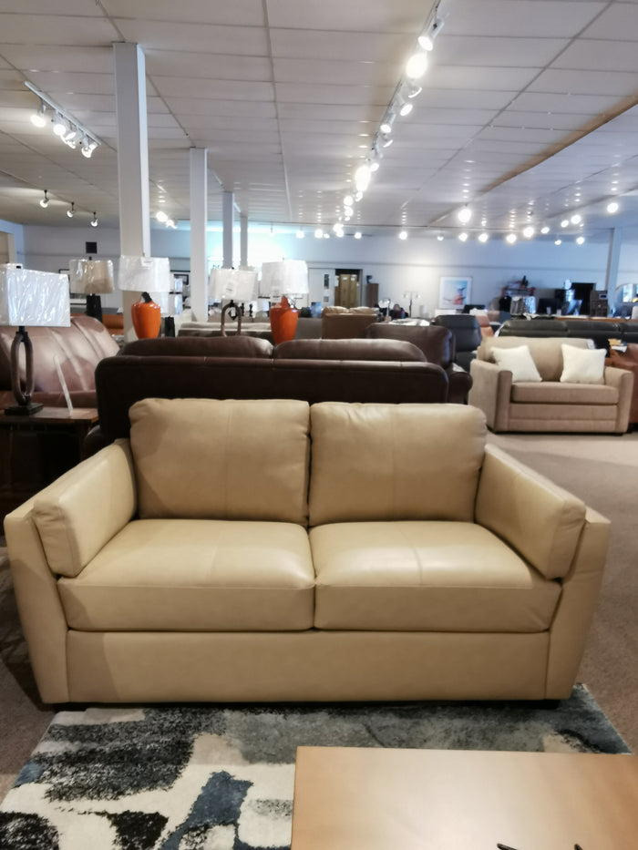 The 77882 Payton Loveseat by Palliser, with a cozy profile, is showcased among sofas and lamps in a showroom.