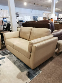 The Palliser 77882 Payton Loveseat, in tan leather with a cozy profile, is displayed amid lamps and modern seating on carpet.