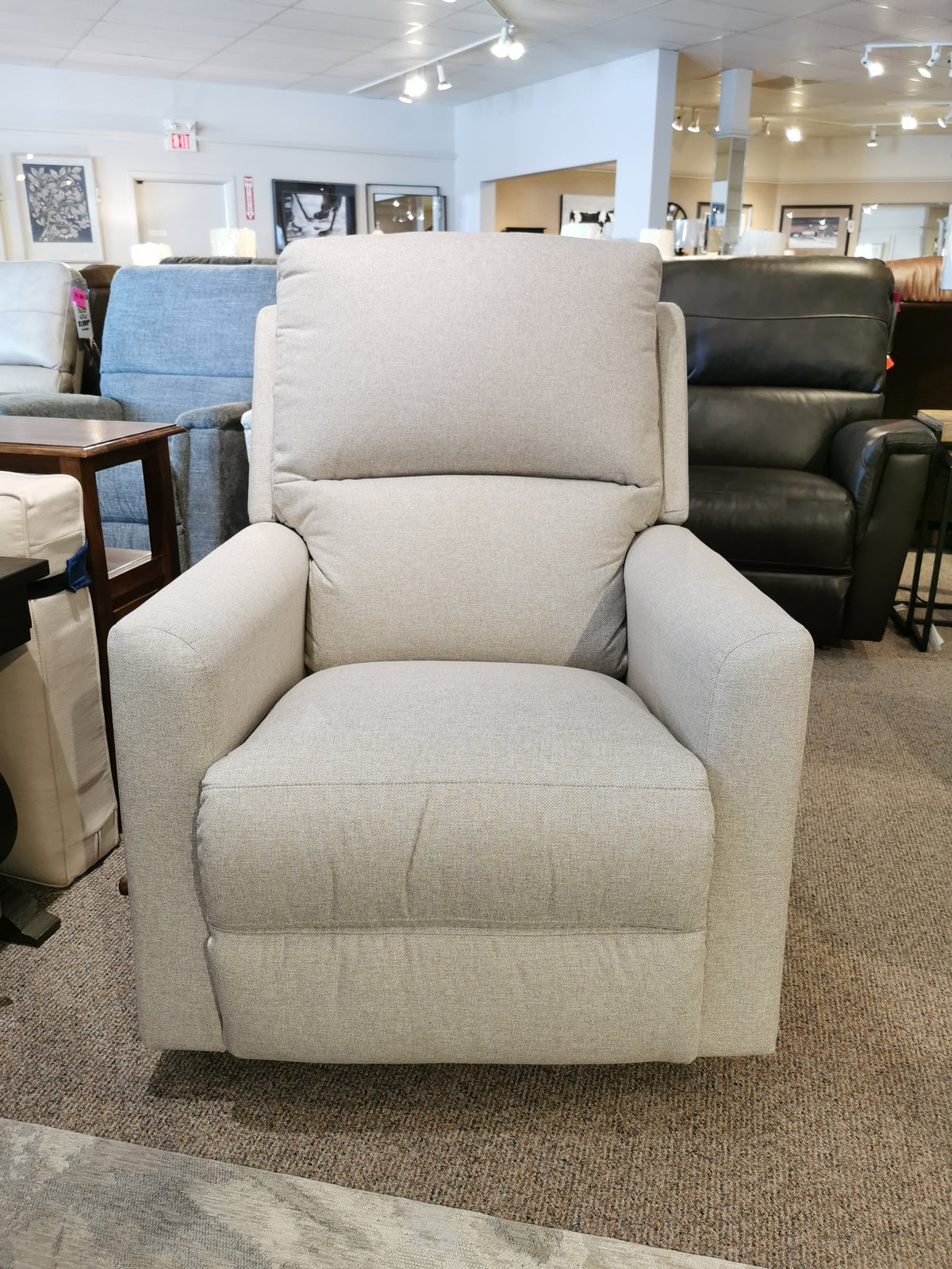 The La-z-boy 700 Wynne Rocker Recliner in gray stands comfortably in a showroom with other furniture around.