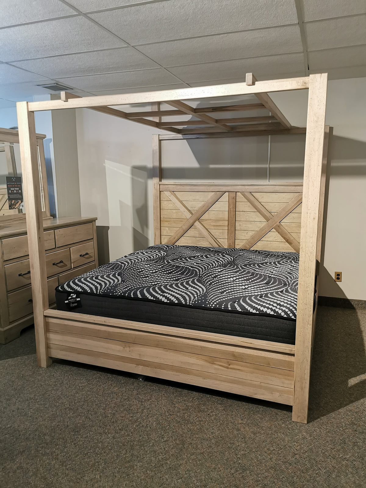 The Vaughn Bassett Cool Rustic King Canopy Bed decorates a room with a patterned mattress, dresser, and beige carpet.