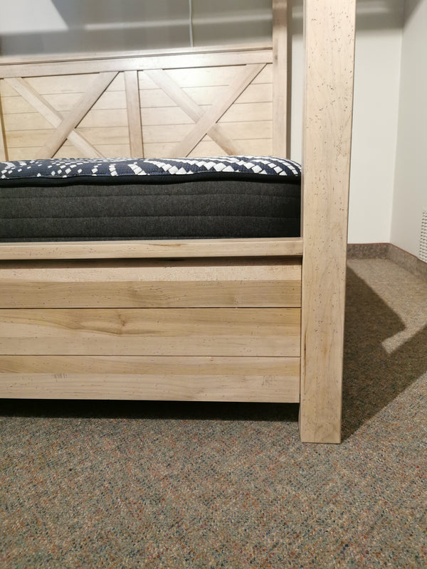 Close-up of the Vaughan Bassett Cool Rustic King Mirrored Canopy Bed with blue and white cover on carpeted floor.