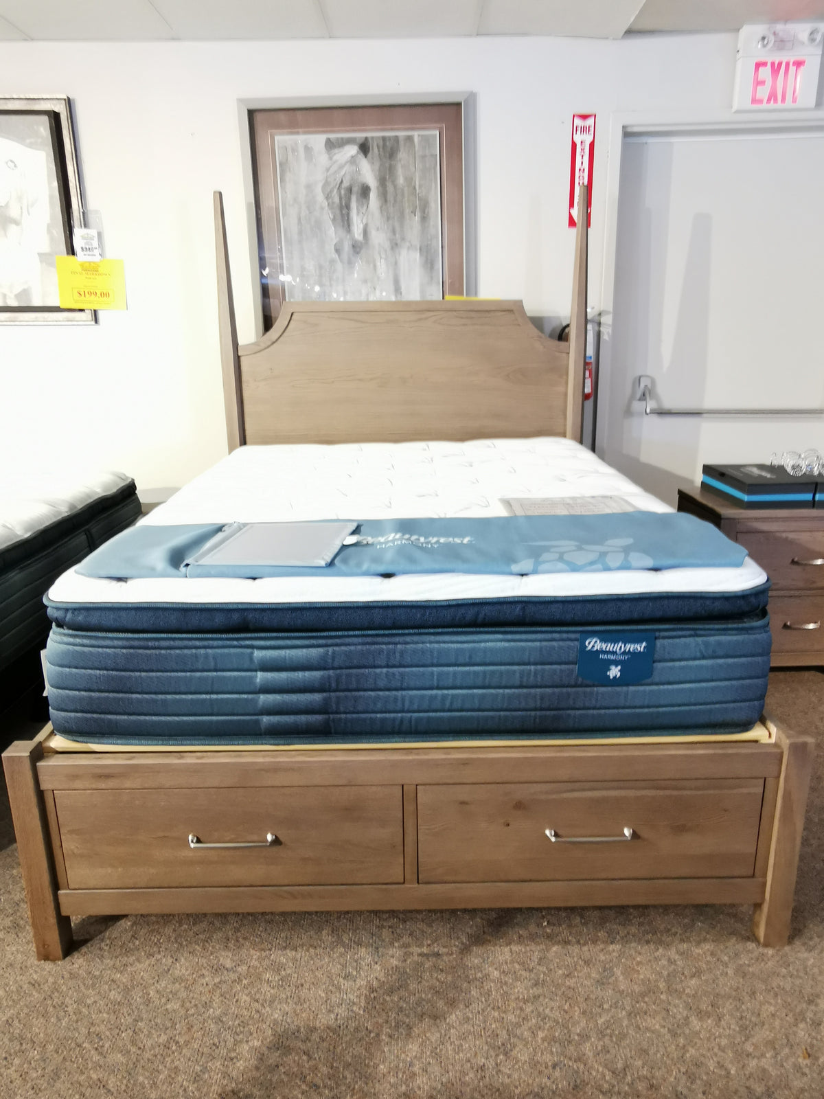 Vaughan Bassett's Pencil Post Tide & Timber Queen Bed in a showroom, features storage drawers and art in the background.