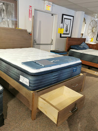 A Vaughan Bassett mattress on a Pencil Post Tide & Timber Queen Bed with an open drawer, shown in the showroom.