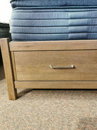 Vaughan Bassett's Oak Pencil Post Tide & Timber Queen Bed features a drawer with a metal handle on a carpeted floor.