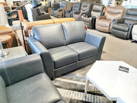 A furniture showroom displaying a range of leather sofas and recliners, highlighted by the classic Bayview Leather Loveseat, a versatile gray two-seater from Leather Craft that stands elegantly in the foreground.