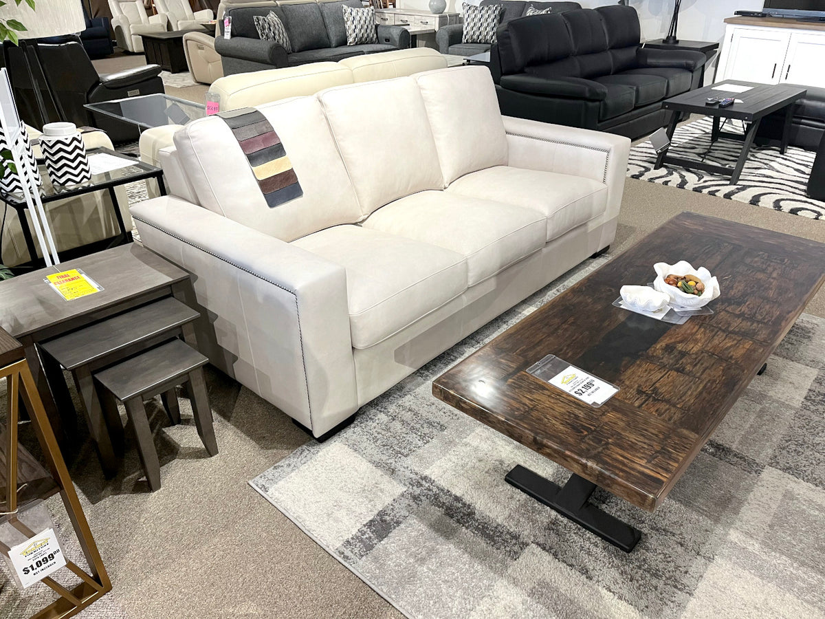 A Gravenhurst Leather Sofa by Leather Craft with a throw is near a wooden coffee table in a showroom surrounded by furniture.