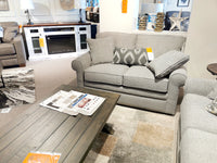 A La-z-boy gray loveseat with patterned pillows next to a rustic wood coffee table in a showroom setting.