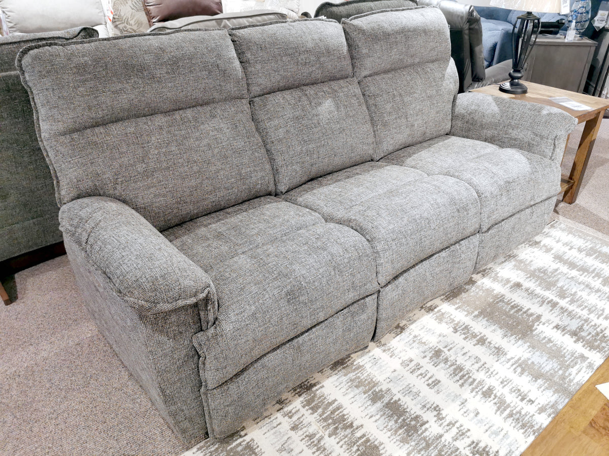 The 706 Jay Power with head-rest Sofa by La-Z-Boy, a gray three-seater featuring thick cushioning and chaise legrests, offers reclining comfort on a patterned rug in the showroom setting.