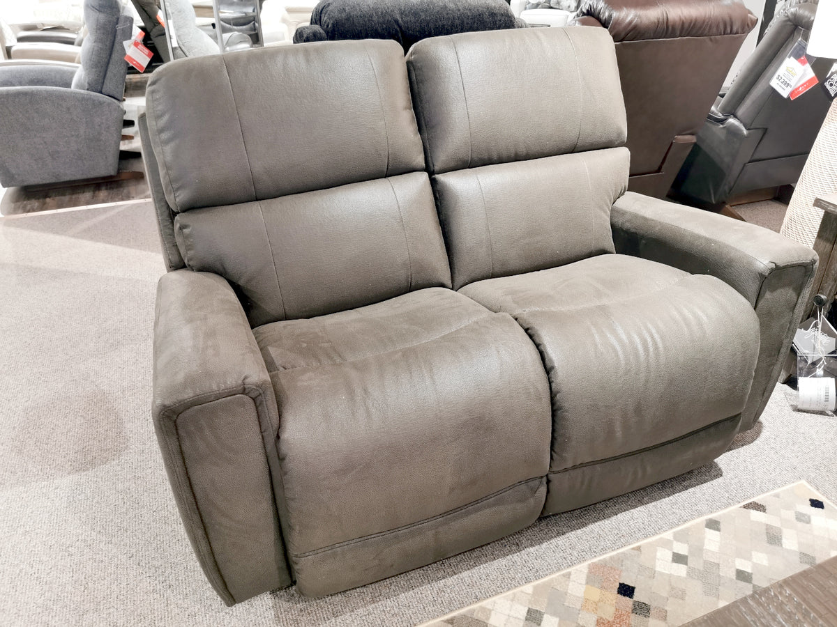 A gray 757 Apollo Reclining Loveseat from La-Z-Boy graces the furniture store showroom, its split backs adding a touch of sophistication amidst various other seats in the background.