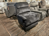 A plush, dark gray 519 Astor Rocker Recliner by La-Z-Boy is on display in a furniture store, surrounded by similar tall recliners on a wooden floor.