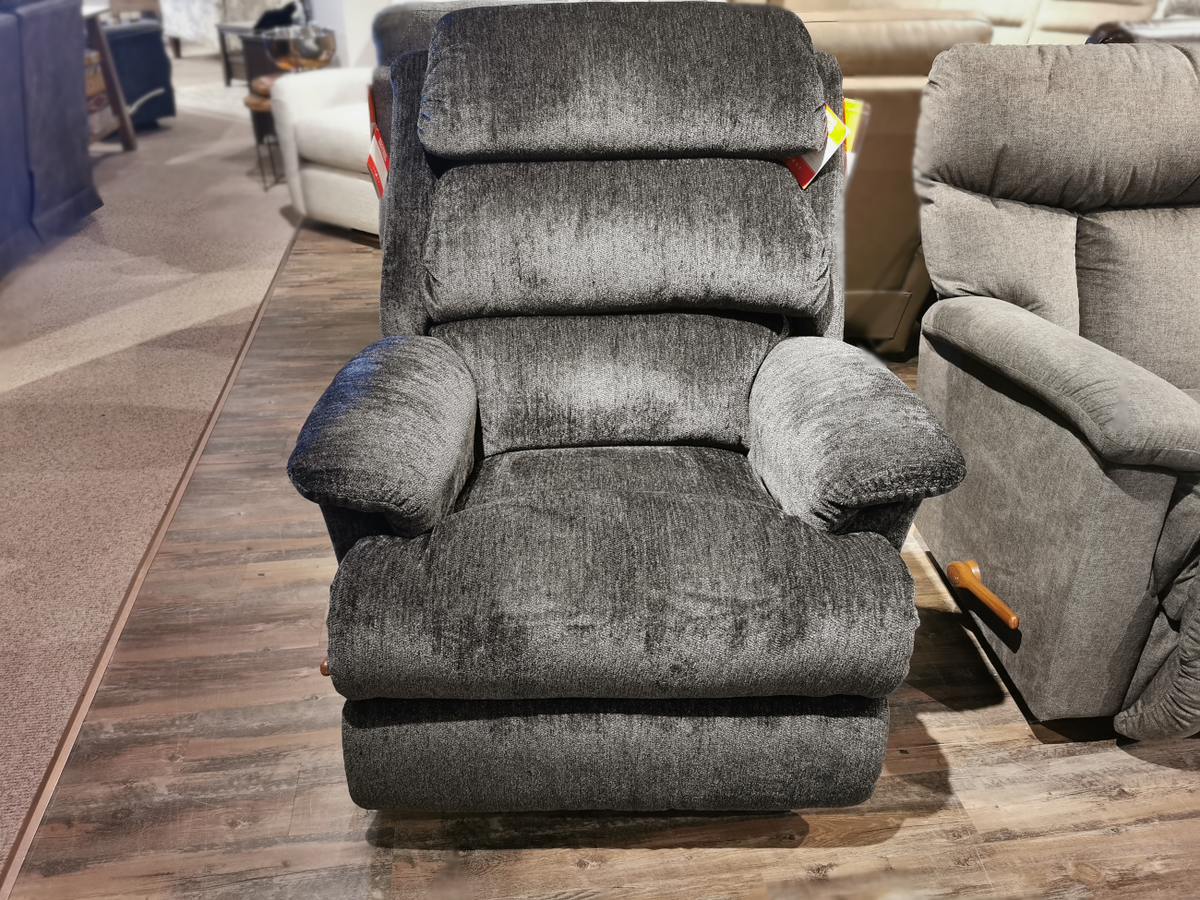 The La-Z-Boy 519 Astor Rocker Recliner, a plush gray piece on the display floor, is nestled among other stylish furniture. This tall recliner promises comfort and elegance in any living space.