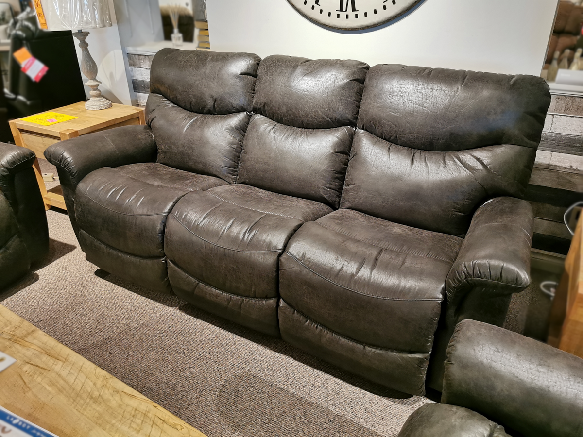 A dark gray leather 521 James Sofa by La-z-boy takes center stage in a cozy living room, paired perfectly with a wooden side table and lamp. Made in America, it seamlessly blends comfort and style for the ultimate relaxation experience.