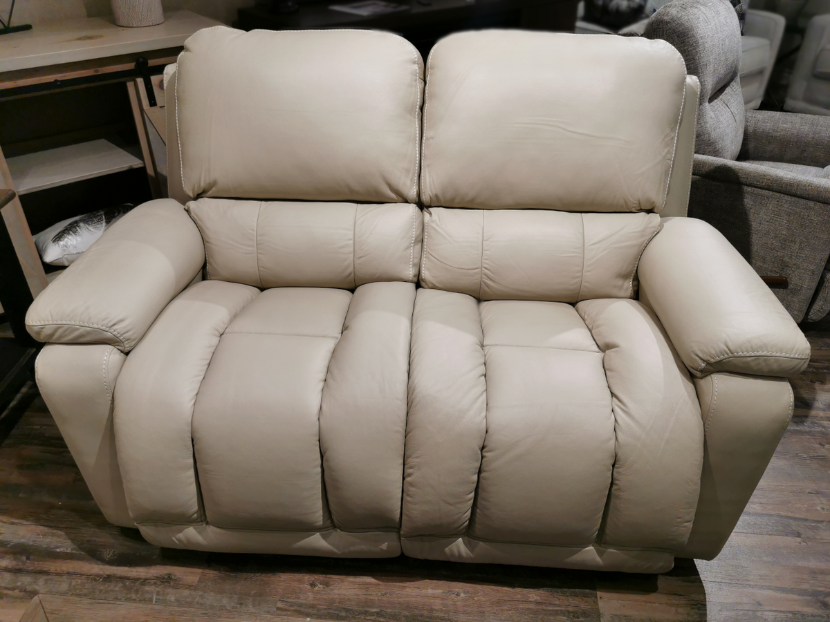 The La-Z-Boy 530 Greyson Reclining Loveseat, with its sleek beige leather and smooth power recline feature, sits elegantly on the wooden floor of a cozy living room.