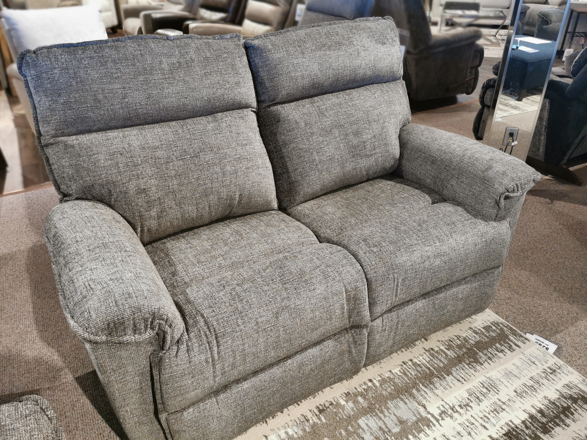 On display in a furniture store is the 706 Jay Power Loveseat with head-rest by La-Z-Boy, featuring a transitional style. This gray loveseat boasts fabric upholstery and plush cushions, providing personalized reclining comfort for those seeking the ultimate in relaxation.