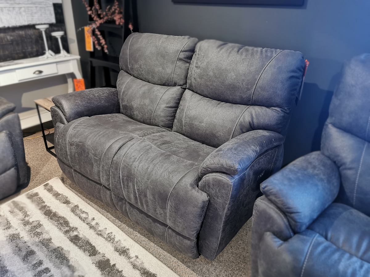 A gray 724 Trouper Loveseat by La-Z-Boy, ideal for family gatherings, is elegantly displayed on a gray and white striped rug in a showroom setting.