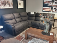 In the showroom, the 724 Trouper Reclining Corner Sectional by La-Z-Boy in dark gray is paired with a wooden coffee table and art on the walls. This sectional offers customizable fabrics, providing a personalized touch.