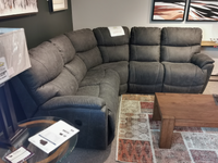 La-Z-Boy's 724 Trouper Reclining Corner Sectional, featuring plush cushions and bucket seats, is showcased in a showroom alongside a wooden coffee table and abstract wall art. Experience unparalleled comfort with the assurance of a limited lifetime warranty.