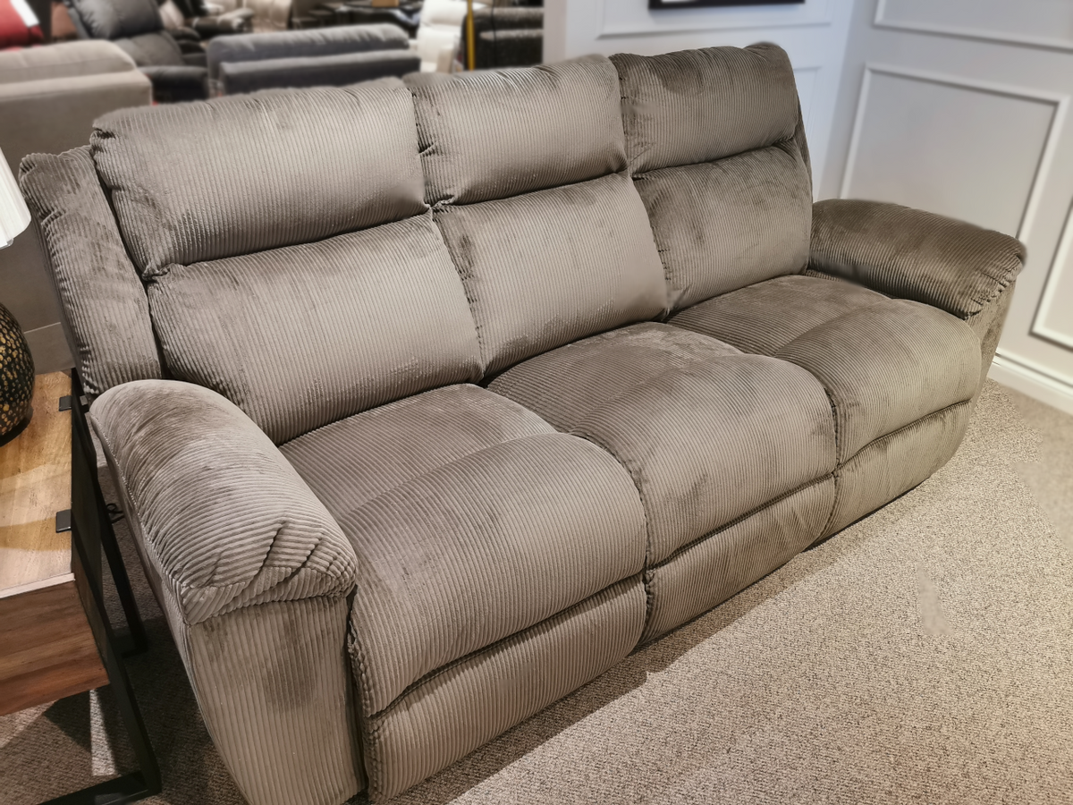 The La-z-boy 761 Joel Reclining Sofa, featuring a refined gray corduroy design with cushioned arm pads, is elegantly displayed on a carpeted floor in the showroom.