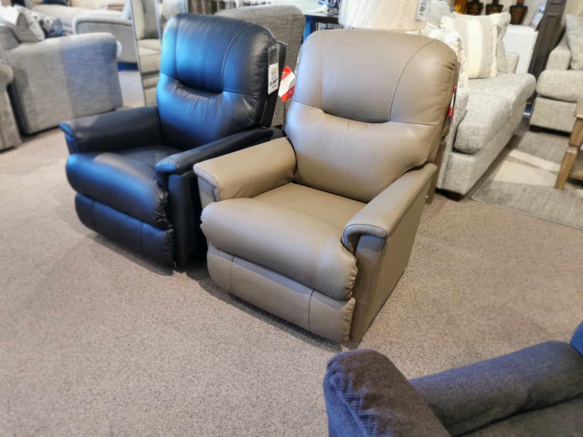 Two 783 Aries Rocker Recliners by La-Z-Boy, featuring one in black and the other in beige with a tufted back, are displayed on a carpeted floor in a furniture store.