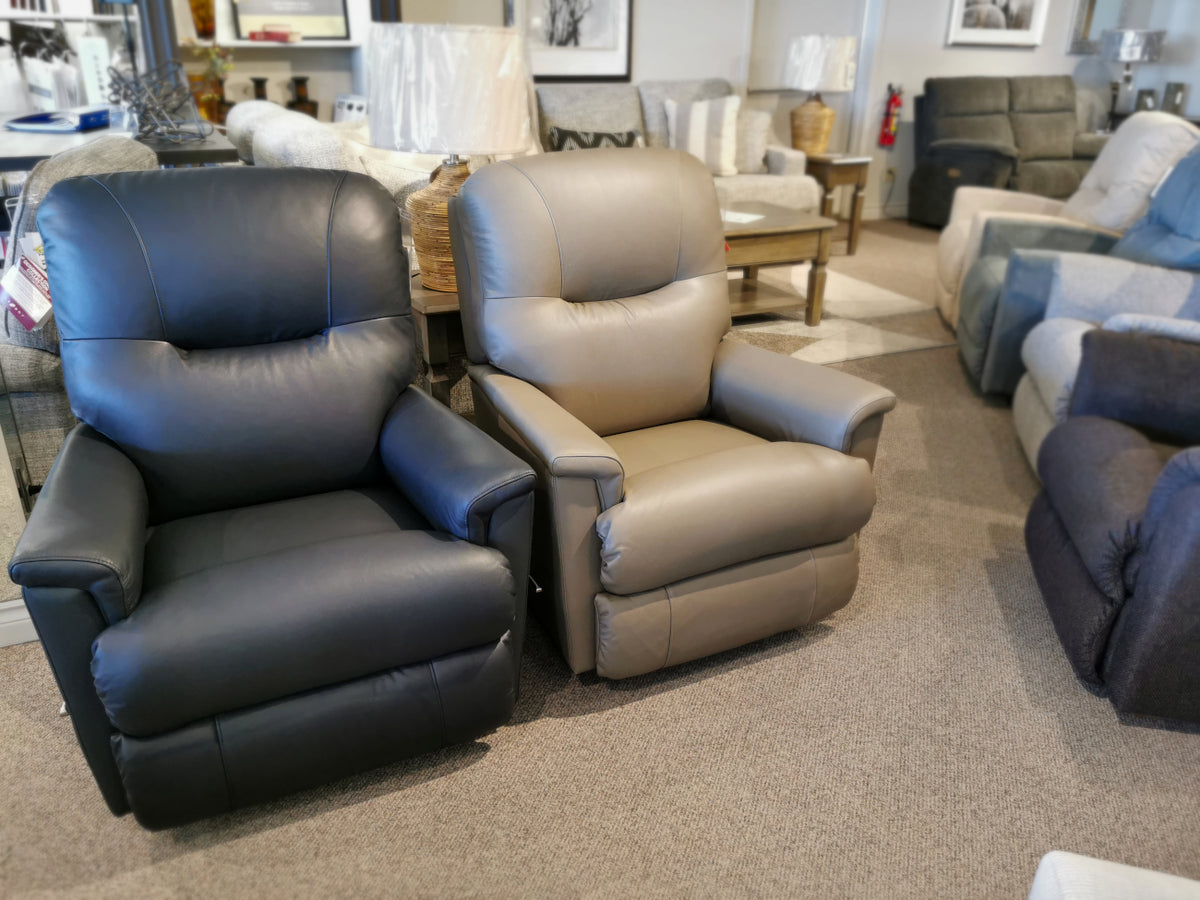 The showroom showcases an elegant selection, featuring the 783 Aries Rocker Recliner by La-Z-Boy in both black and beige. These tufted back rocking recliners include the option of a power adjustable headrest on the beige model, all displayed amidst an array of other exquisite furniture pieces.