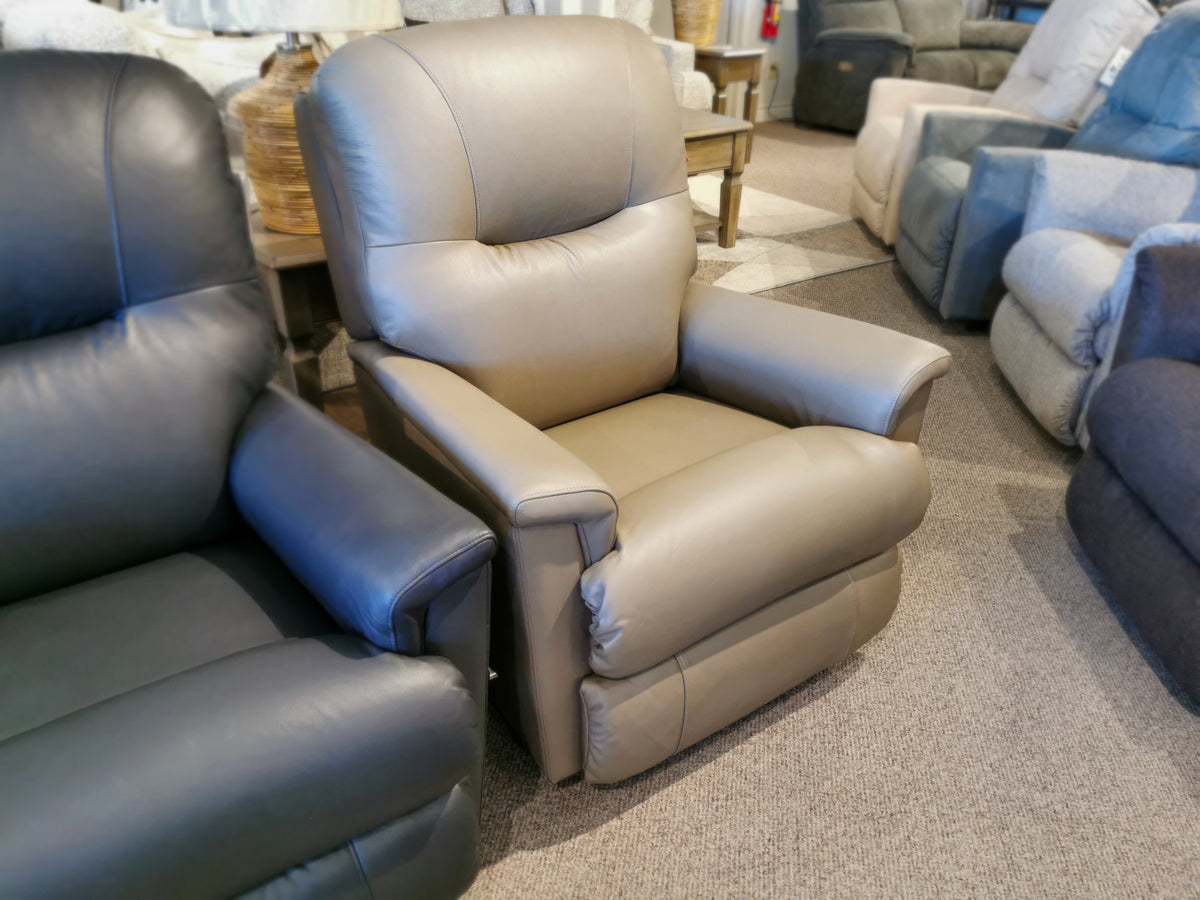 A 783 Aries Rocker Recliner by La-Z-Boy in beige leather is elegantly placed next to a dark leather reclining rocker on the showroom floor, highlighting exceptional comfort and durability.