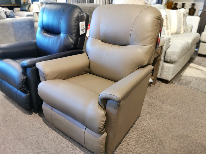 The 783 Aries Rocker Recliner, a light brown leather chair with an adjustable headrest from La-Z-Boy, is showcased in a furniture store, surrounded by other sofas in the background.