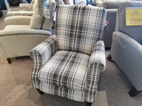 The La-Z-Boy 931 Charlotte High Leg Recliner, featuring a plaid pattern in beige, black, and white, is showcased in a furniture store. It offers customizable fabrics for a personalized touch.