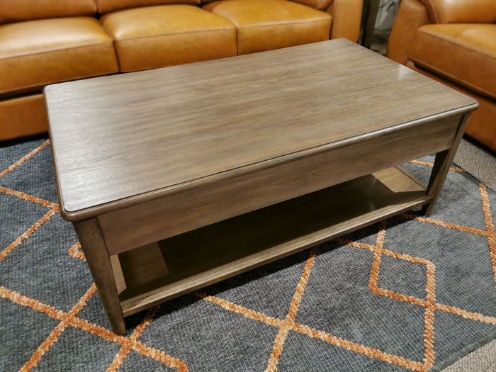 From the Magnussen collection, the T5695-50 Corden Lift Top Coffee Table, featuring a wooden design with a hickory veneer and practical shelf, stands elegantly on a geometric-patterned rug, surrounded by brown leather sofas.