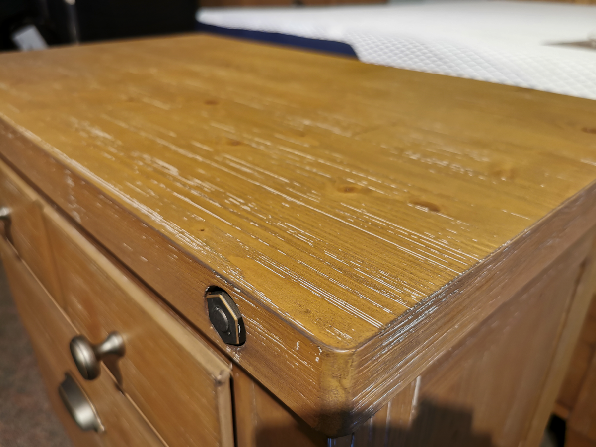 Close-up of a corner from the B5487 Lynnfield Nightstand by Magnussen, featuring a weathered fawn finish complemented by metal knobs and highlighting its textured grain.