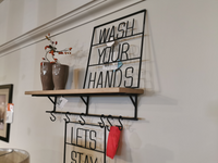 The Mercana 68493 Schutt Shelf, a modern wall-mounted piece crafted from Indian mango wood, includes vases and metal signs that read "WASH YOUR HANDS," along with convenient hooks underneath.