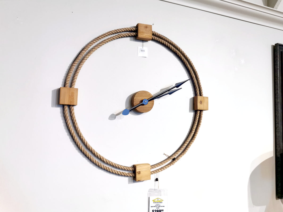 The 68527 Worthing Wall Clock by Mercana, featuring an open-face design with wood and rope accents and striking blue hands, is displayed against a white wall.