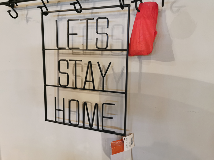 Adorn your walls with Mercana's 69329 Let's Stay Home metal cut-out quote, featuring a striking red bag for an enchanting addition to your home decor.