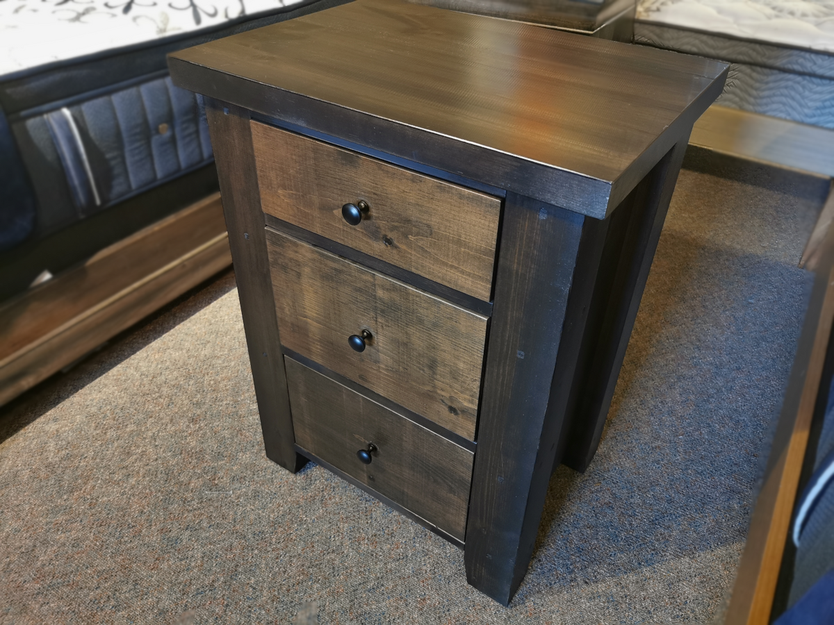 Munros 3 Drawer Pine Nightstand with round handles, displayed on a carpeted showroom floor.