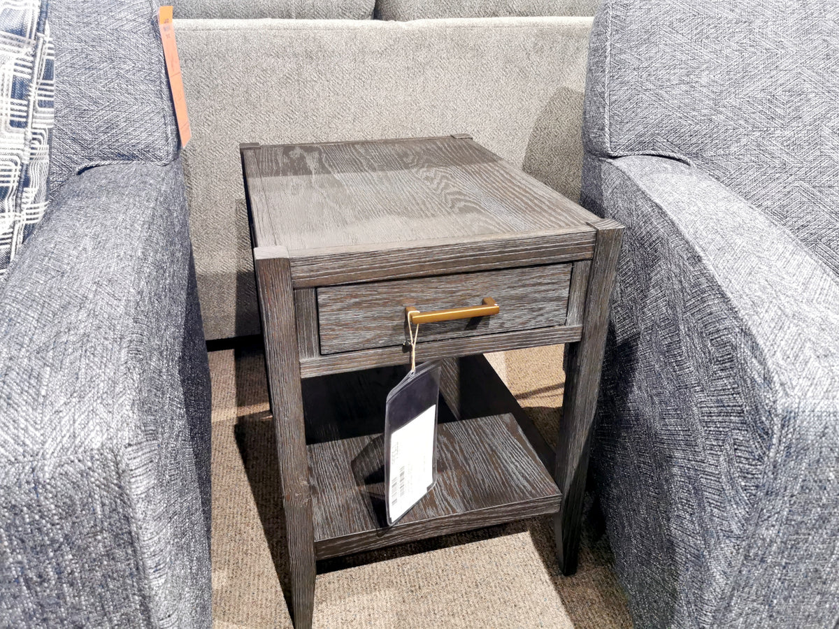 A Null Furniture Manhattan 1022 end table with dark oak veneer and brass hardware sits between two gray upholstered chairs.