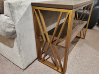 The Westchester 1321 Sofa Table by Null Furniture features an ash veneer top and gold geometric frame next to a beige sofa.