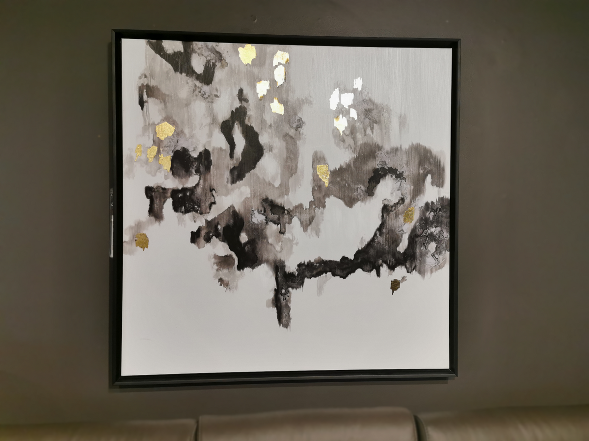 The Black Gold Abstract (foil) Canvas Frame by Picture Depot, featuring hand-embellished black, gray, and gold tones, is elegantly encased in a sleek black frame and adorns a dark wall above a gray couch.