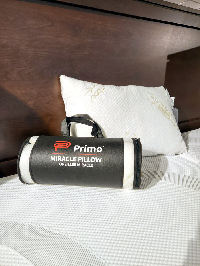 A packed pillow from Primo's Miracle Pillow collection sits on a bed, while its twin with shredded memory foam rests unpacked in the background.