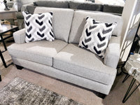 The Superstyle 9671 Loveseat, a contemporary gray sofa with patterned pillows, sits on a carpet in the showroom.