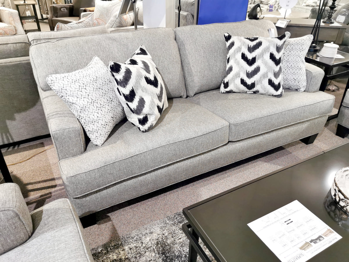 A Superstyle 9671 Loveseat with patterned pillows highlights modern design beside a coffee table in the showroom.