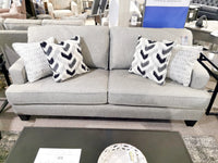 The Superstyle 9671 Loveseat features a contemporary gray design with patterned cushions behind a glass coffee table.