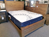 The Vaughan Bassett 752 Dovetail Queen Poster Bed with a patterned mattress is showcased among dressers in a furniture store.