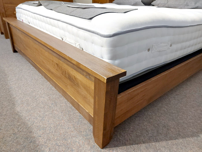 The Vokes 250 Rough Sawn King Bed, featuring a single panel footboard and accompanied by a white mattress, rests elegantly on a beige carpeted floor, highlighting its rustic charm with a provincial finish.