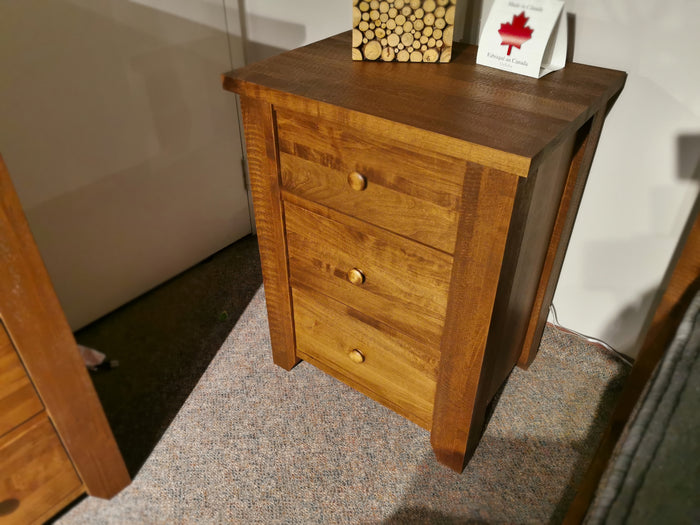 Vokes' 250 Roughsawn 3-Drawer Night Table features a stacked log decoration and framed Canadian-themed artwork on top, offering provincial finishes that enhance its rustic charm. The warm maple undertones bring a cozy touch to any room.