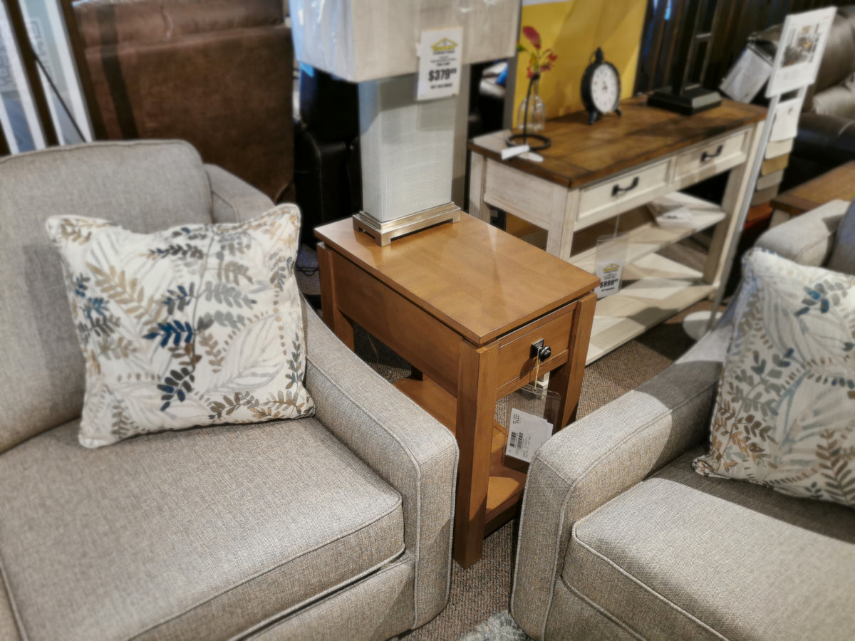 The Ingleton 14" Lamp Table by Winners Only in light walnut stain sits between two gray sofas with floral pillows.