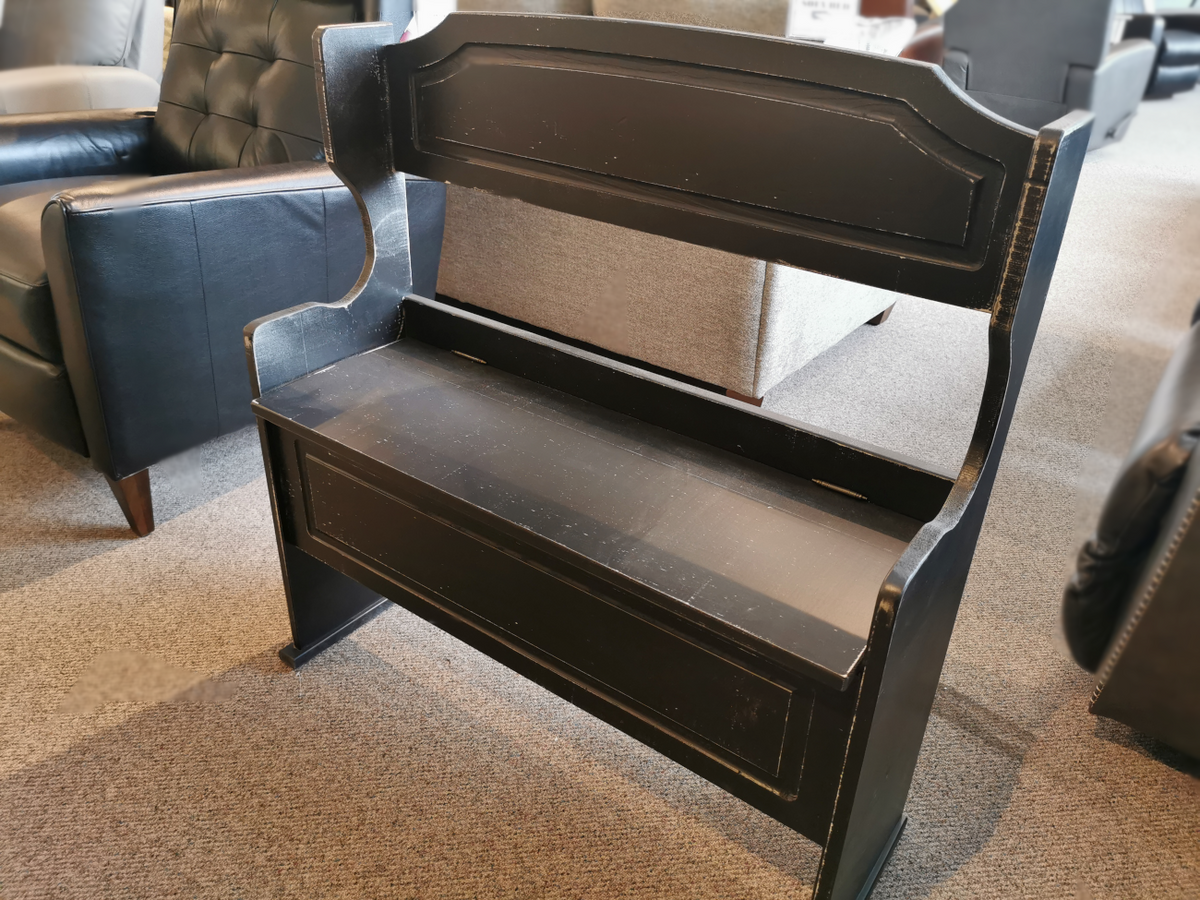 The Woodcraft 401 Panel Bench, a sleek bench with a high backrest and storage compartment in a black design, is showcased in a furniture showroom.