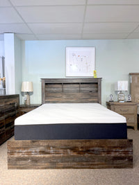 Create a stylish rustic industrial bedroom setup with the Ashley B211 Drystan Queen Bookcase Bed featuring convenient storage drawers, a comfortable mattress, two elegant nightstands complete with lamps, and striking wall art to complete the room.