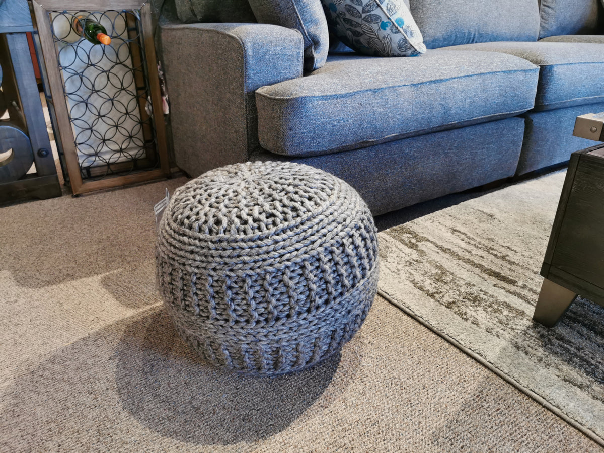 The Ashley A1000559 Benedict Pouf graces the carpet beside a gray couch in a cozy living room.