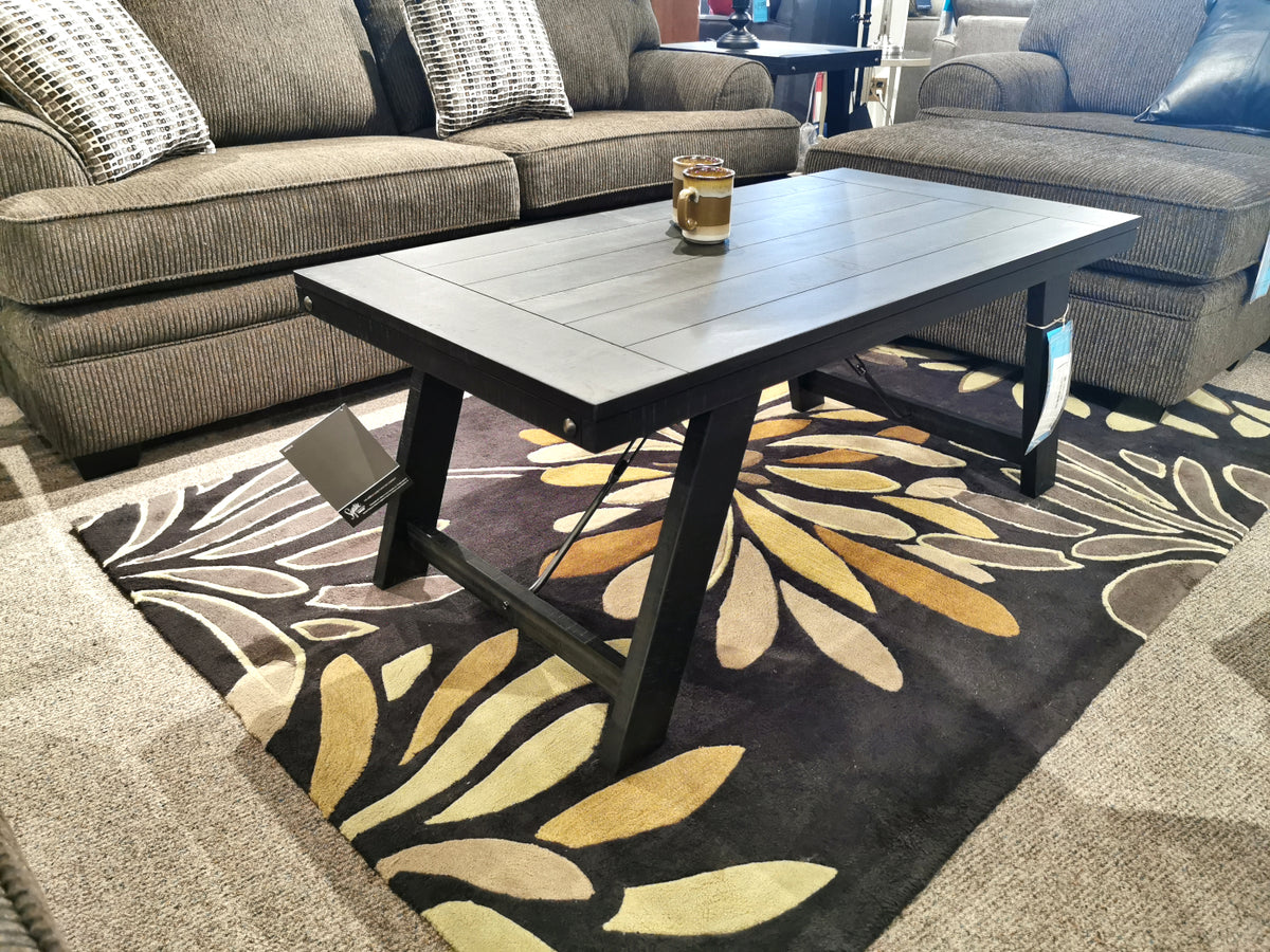 The T351 Noorbrook Table Set by Ashley features a distressed black wash finish for a farmhouse look on the floral rug.