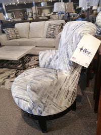 The Best 2968E Justine Swivel Chair with a high back and patterned fabric is in a showroom with sofas and a coffee table.