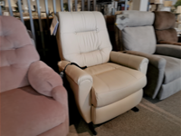 A beige Felicia Lift Chair from the brand Best, featuring modern design elements, is showcased between a pink chair and a grey chair in a furniture store setting.